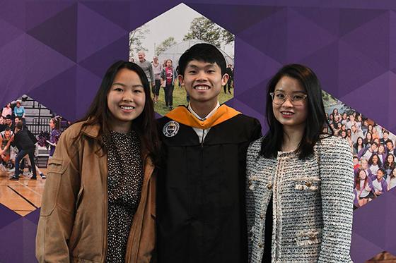 A graduating student in robes poses with two family members, all of whom are smiling broadly on Commencement Day